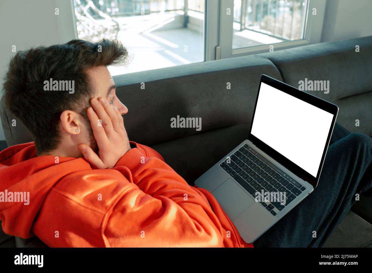 Le jeune adulte est choqué par ce qu'il voit sur l'ordinateur portable, l'ordinateur portable avec écran blanc vierge et le texte prêt pour le placement Banque D'Images
