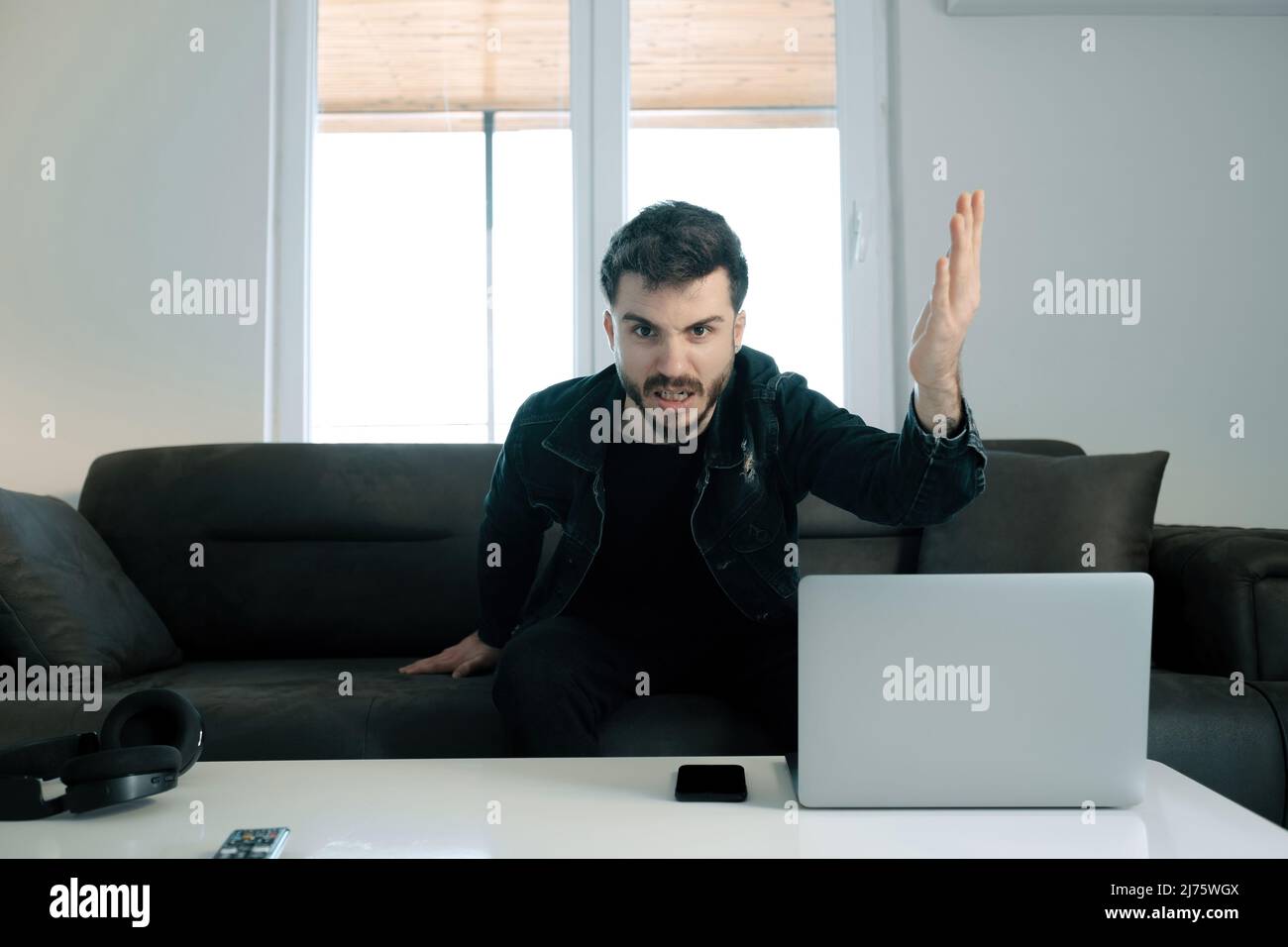 Frustré jeune homme, homme assis sur le canapé dans le salon et se fâcher à la caméra, il est très en colère avec le résultat du match et le montre avec Banque D'Images