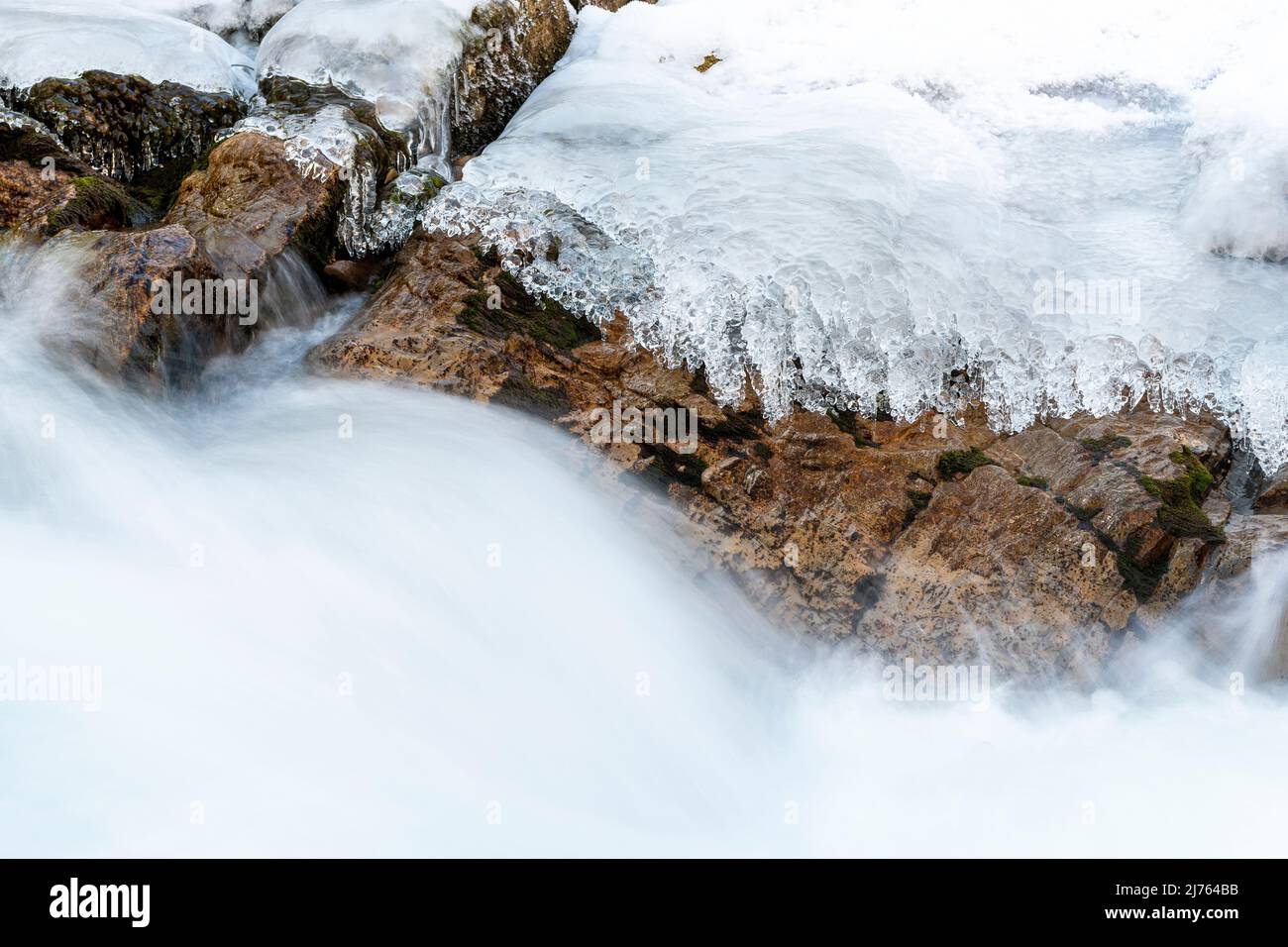 L'eau rapide du Rissbach forme du jet et du courant. Les structures de glace et les rochers formés sur la rive du ruisseau de montagne, bordent l'image. Pris en hiver au Tyrol, en Autriche dans l'Eng, près de l'Ahornboden. Banque D'Images