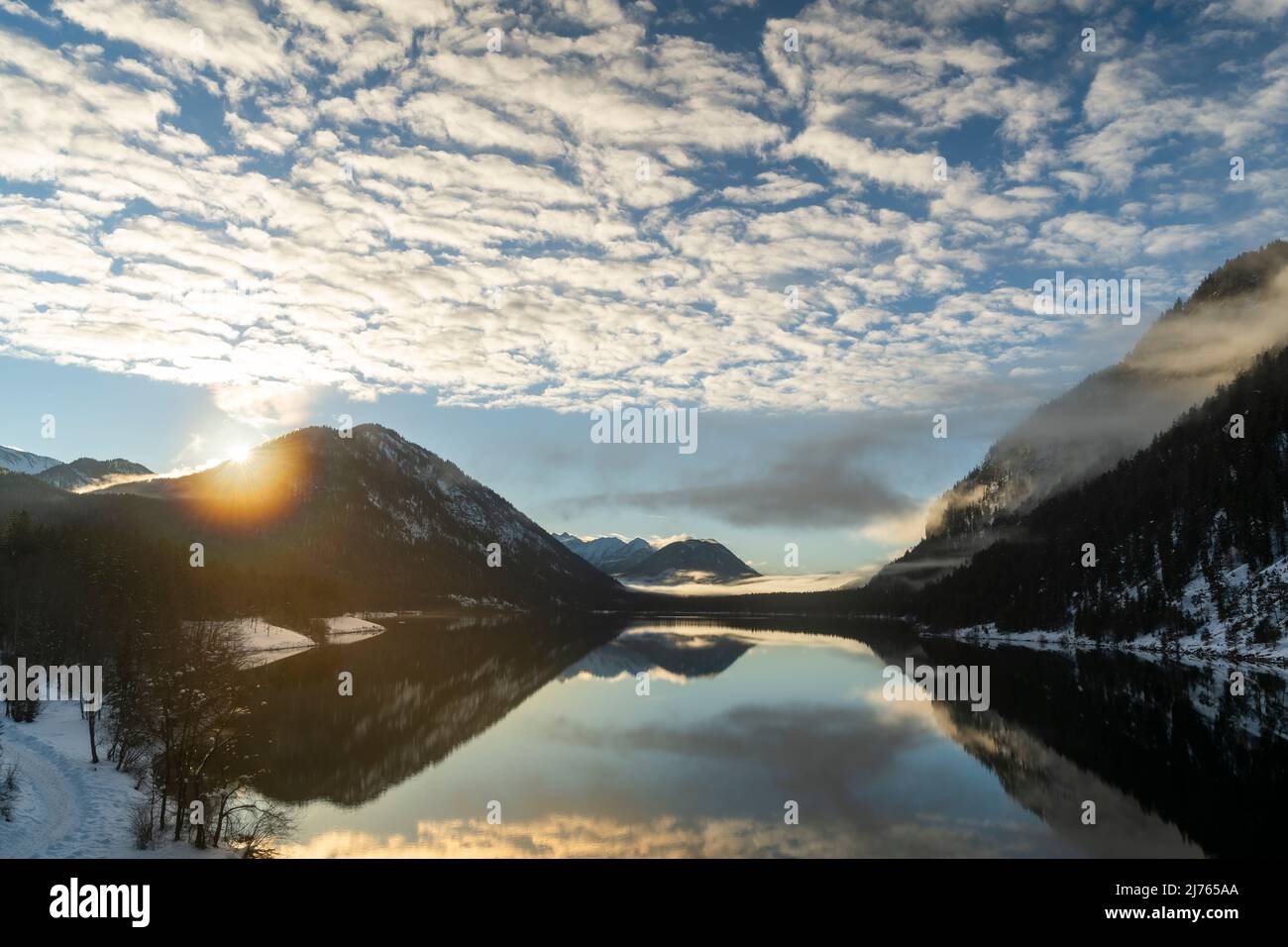 Le soleil du soir en hiver sur la rive du réservoir de Sylvenstein. Nuages inetressant et atmosphère de brouillard comme un reflet dans l'eau claire du lac alpin dans les Alpes bavaroises au bord du Karwendel. Banque D'Images Le soleil du soir en hiver sur la rive du réservoir de Sylvenstein. Nuages inetressant et atmosphère de brouillard comme un reflet dans l'eau claire du lac alpin dans les Alpes bavaroises au bord du Karwendel. Banque D'Images