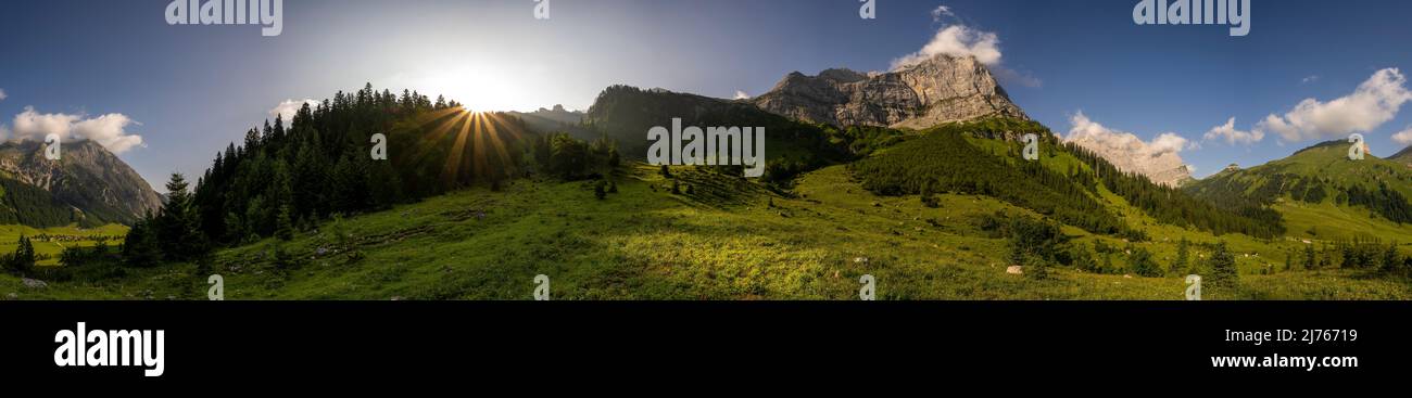 Lever de soleil sur le sentier panoramique de randonnée de Binsalm dans l'Eng, au coeur du Karwendel dans le Tyrol. Le soleil levant évoque une étoile et fait briller l'herbe fraîche du début de l'été. Les tours de Lamsenspitze (2508m) en arrière-plan. Banque D'Images