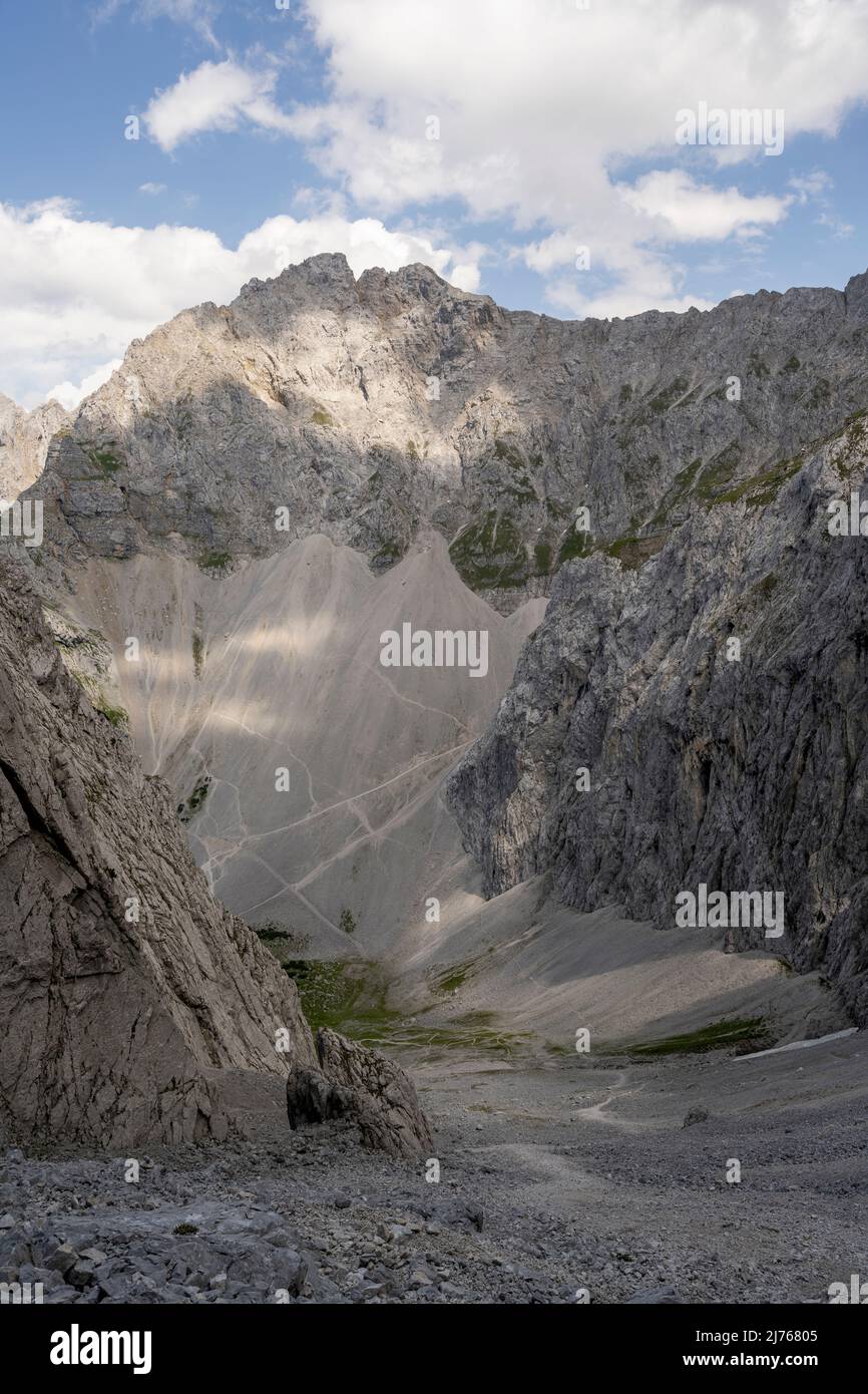 Vue à travers le Viererscharte au-dessous du Viererspitze (2054m) dans le Karwendel au-dessus de Mittenwald, jusqu'au célèbre Dammkar. La zone rugueuse de roche et de désert de pierre est seulement décomposée par le ciel bleu avec quelques nuages. Banque D'Images