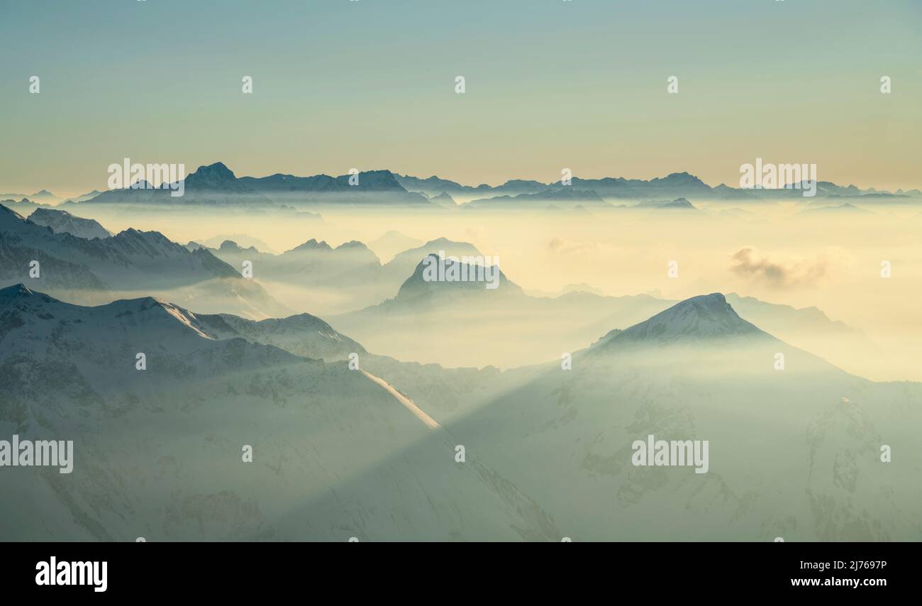 Paysage alpin de montagne au-dessus de la brume dans la lumière chaude du soleil couchant en hiver. Vue depuis Widderstein jusqu'aux montagnes de Lechquellen. En arrière-plan, les Alpes de Sesaplana et Glarner avec Tödi. Vorarlberg, Autriche, Suisse, Europe Banque D'Images