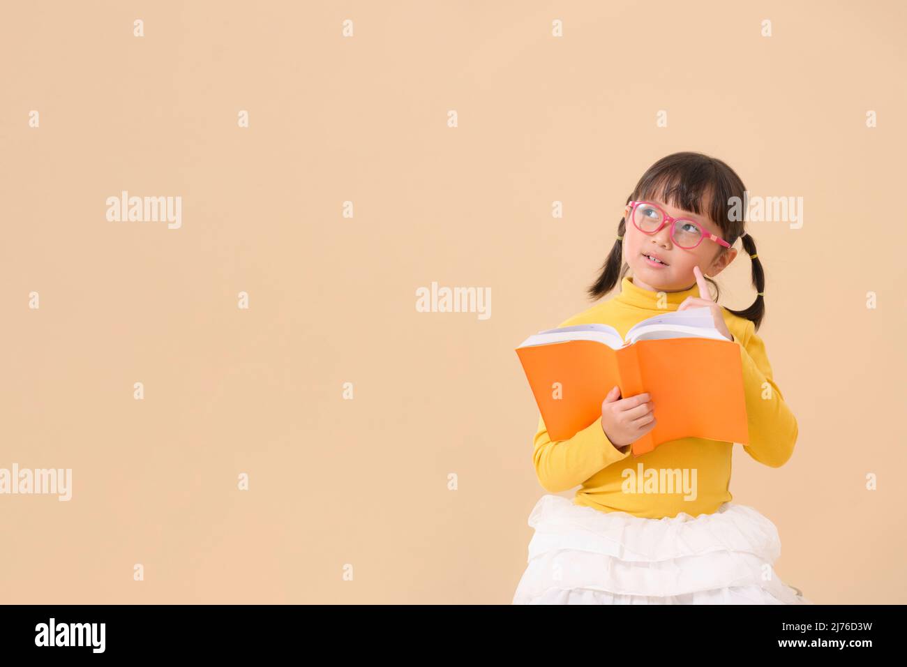 Adorable et joyeux enfant asiatique petite fille portant des lunettes lecture intéressant livre pensant impliqué dans l'éducation Banque D'Images