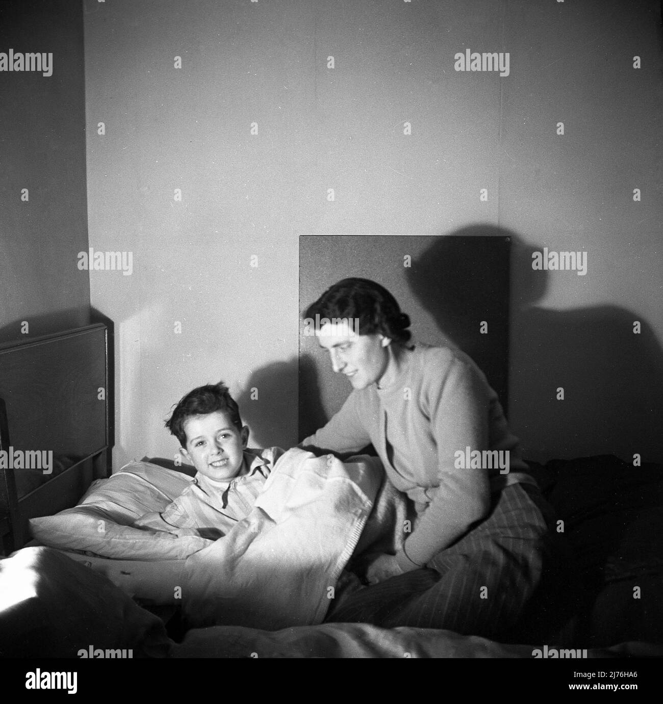 1950s, historique, la Grande-Bretagne d'après-guerre et une mère voyant son jeune fils se coucher. Banque D'Images
