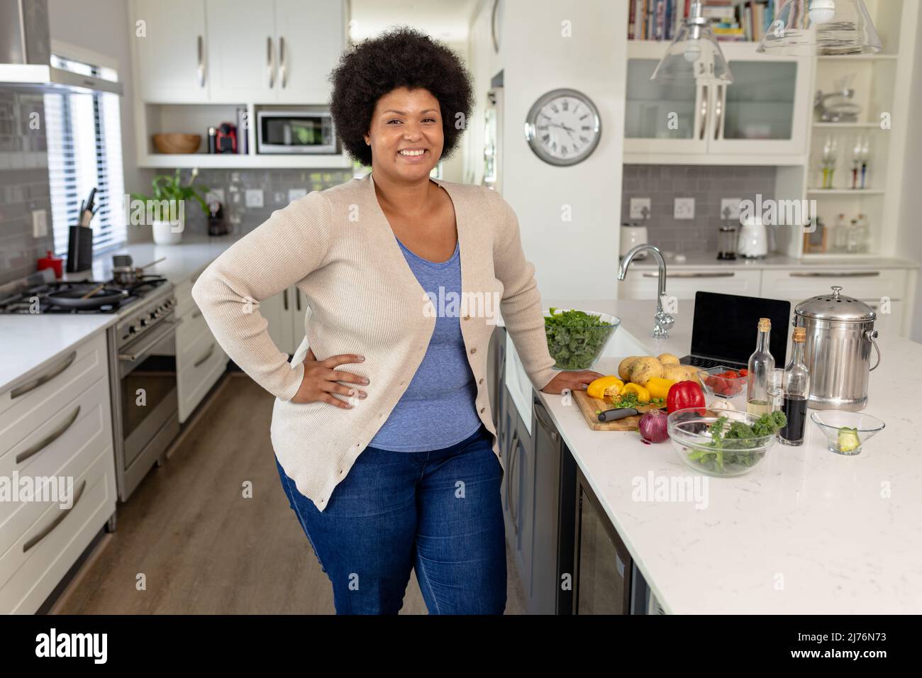 Portrait d'une femme mi-adulte afro-américaine souriante avec main sur la hanche debout dans la cuisine à la maison Banque D'Images