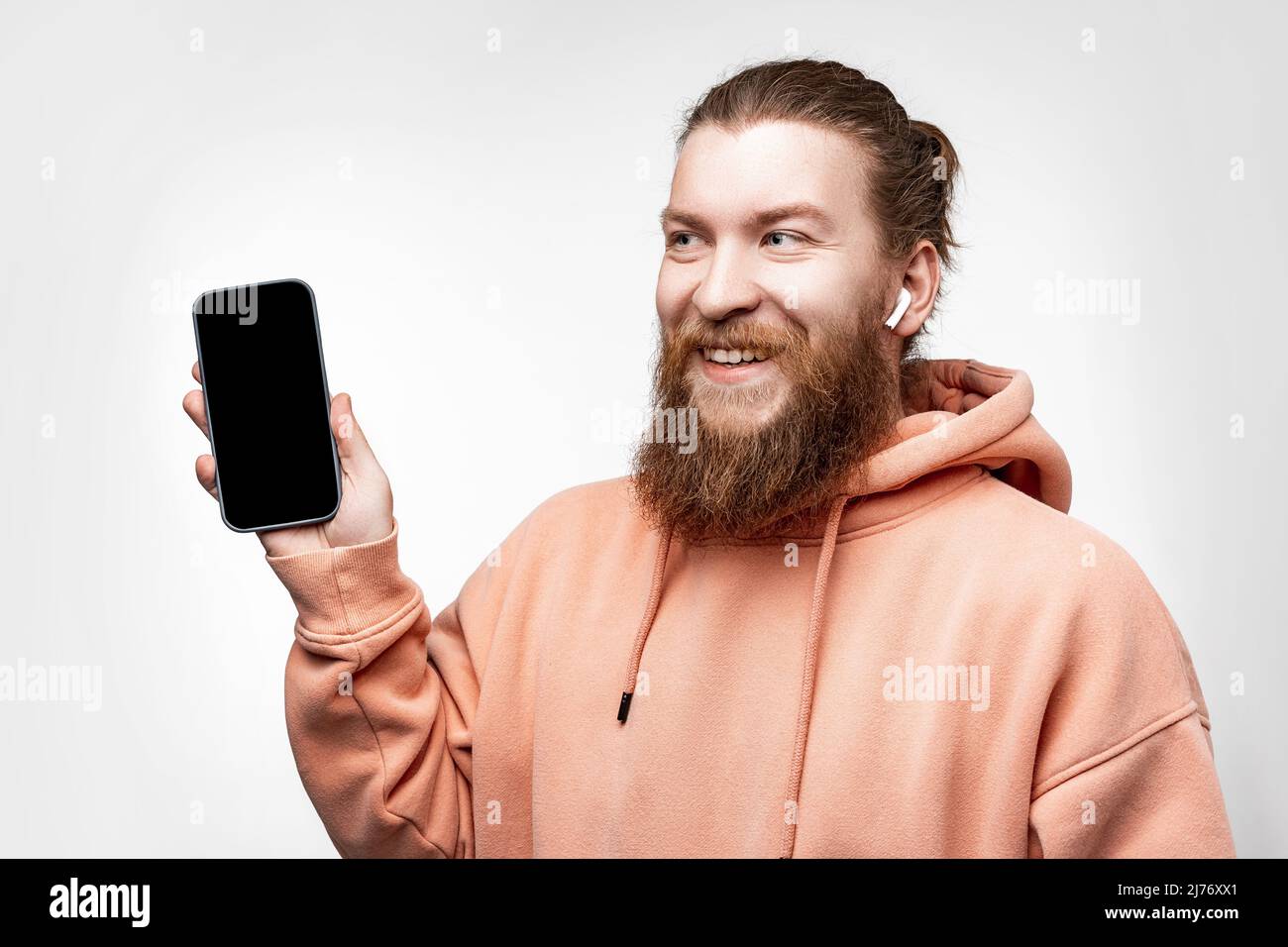 Homme de bonne humeur scandinave tenant un téléphone avec écran noir et casque sans fil isolé sur fond gris. Gars avec gingembre coiffé Banque D'Images