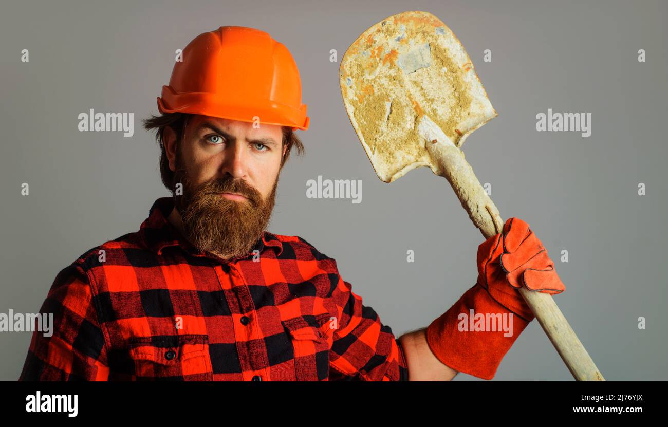 Ouvrier de construction barbu en casque avec bêche. Gants de travail de construction avec pelle. Banque D'Images