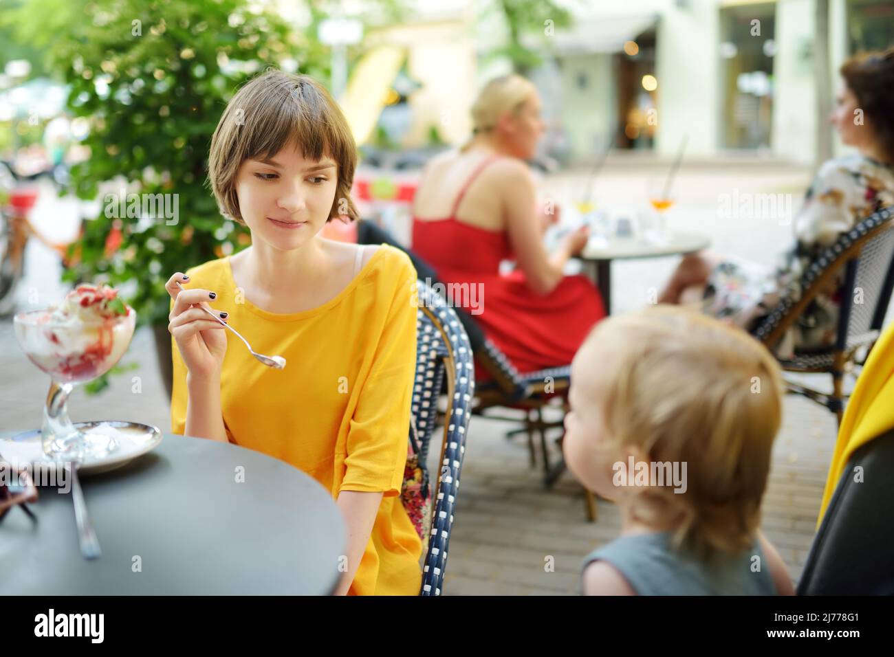 Jolie jeune fille qui mange de la glace fraîche savoureuse à l'extérieur le jour ensoleillé de l'été. Grande sœur qui nourrit un dessert à son frère tout-petit. Bonbons pour enfants. Banque D'Images