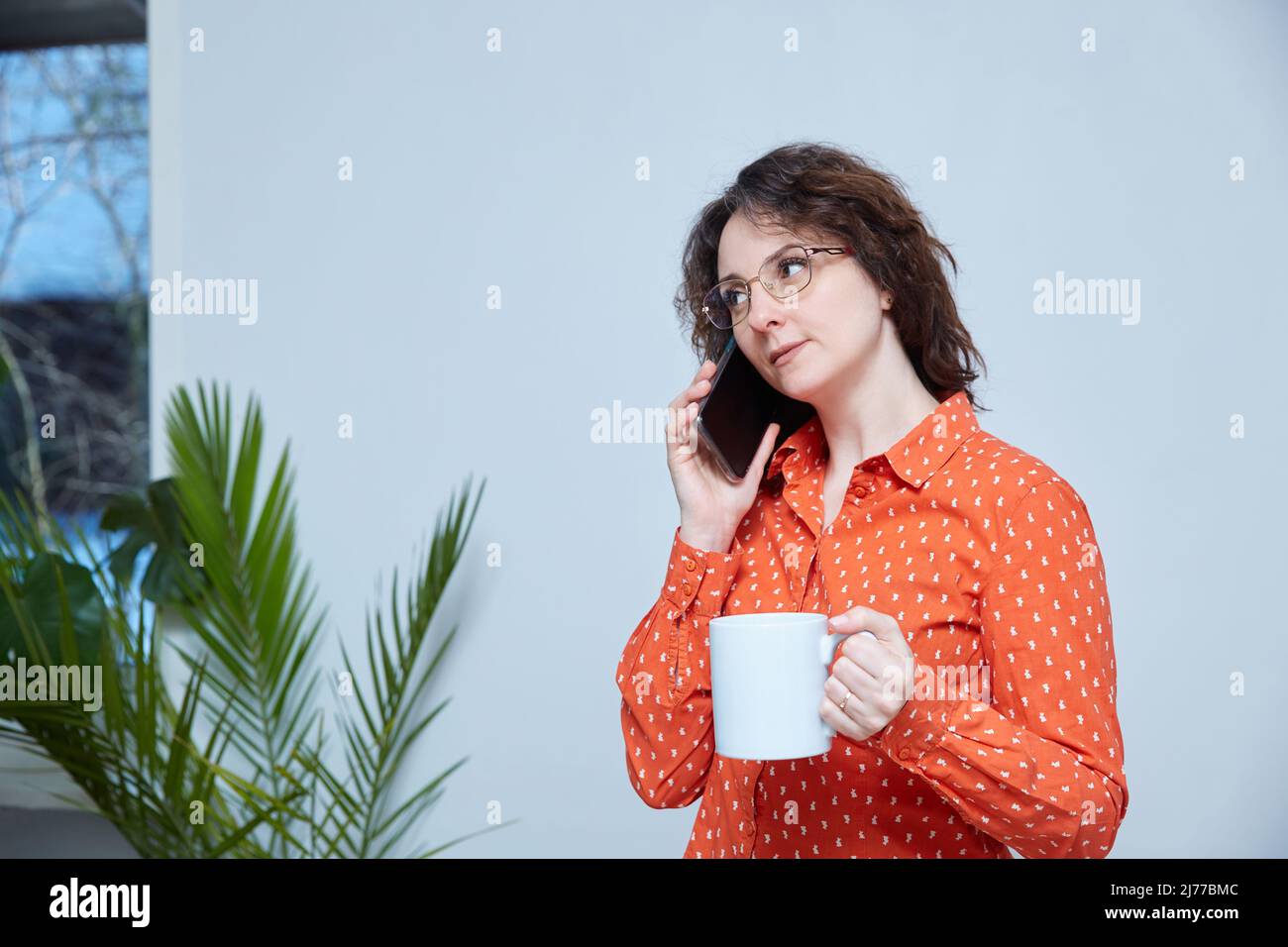 Une femme d'âge moyen parle au téléphone à la maison. Contient le gobelet Banque D'Images