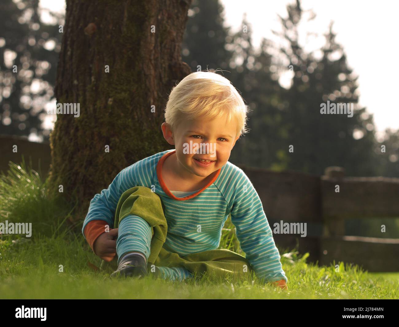 garçon assis dans l'herbe et en riant à la caméra Banque D'Images