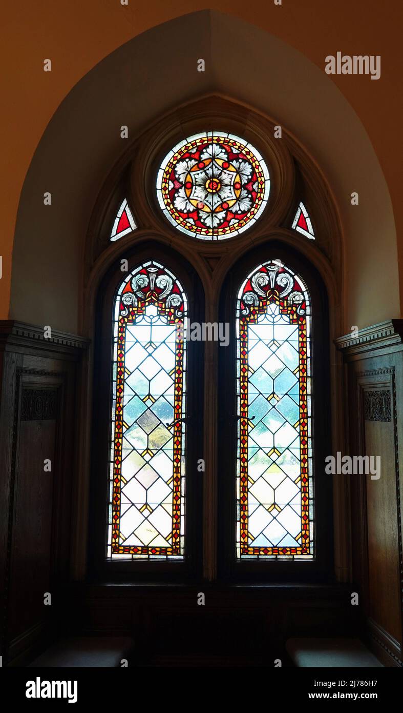 Une belle fenêtre en vitraux gothiques dans un ancien manoir. Il y a des sièges sous la fenêtre. Les murs sont épais Banque D'Images