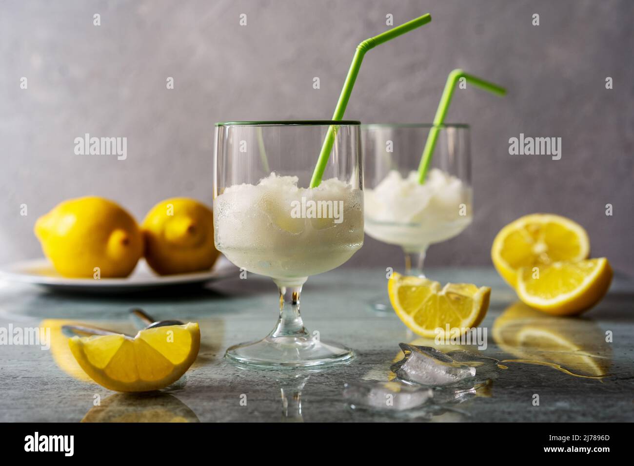 Sorbet citron dans deux verres avec citrons, glaçons et pailles à boire sur fond gris Banque D'Images