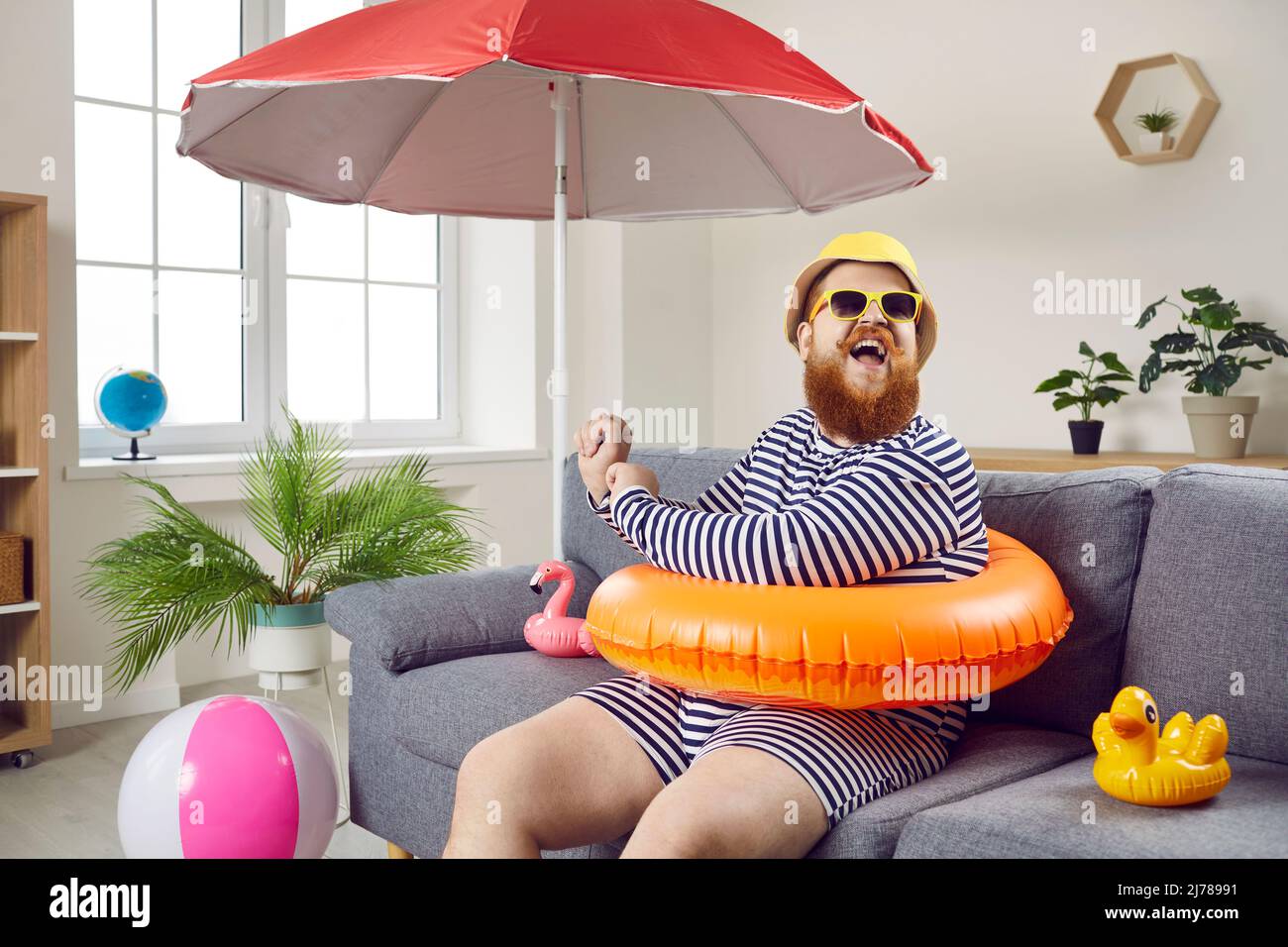Drôle de chubby homme ayant l'amusement assis sur le canapé dans le salon avec le cercle gonflable de natation. Banque D'Images
