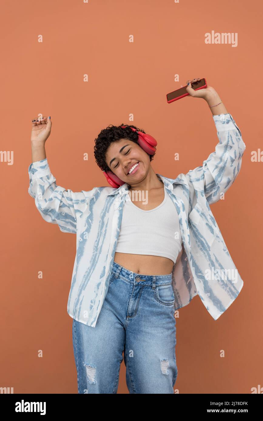 Portrait d'une jeune femme latine heureuse avec un smartphone et des écouteurs dansant dans la rue, Panama, Amérique centrale Banque D'Images