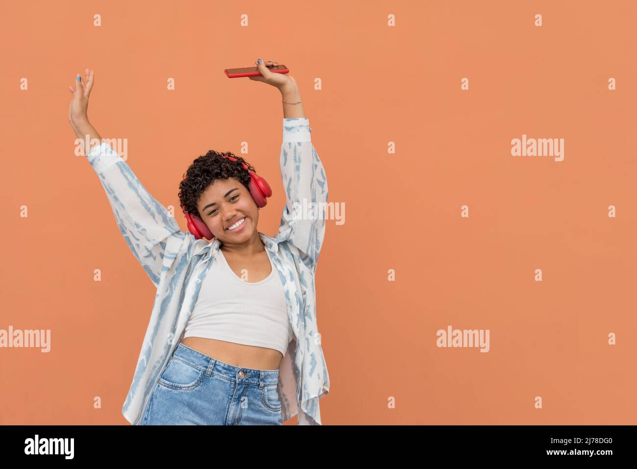 Portrait d'une jeune femme latine heureuse avec un smartphone et des écouteurs dansant dans la rue, Panama, Amérique centrale Banque D'Images