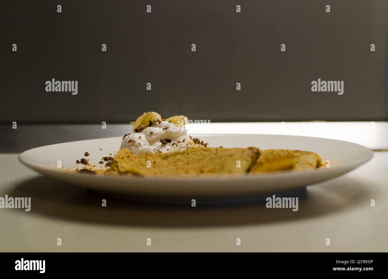 Parsemez les crêpes avec des morceaux de banane sur la crème fouettée sur la plaque blanche, en gros plan Banque D'Images