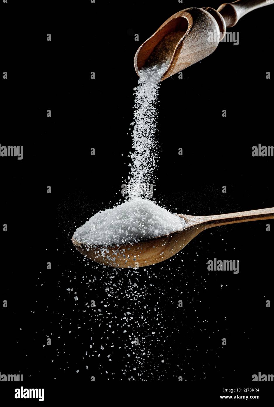 Cristaux de sucre blanc raffiné tombant dans la cuillère en bois sur fond noir. Banque D'Images