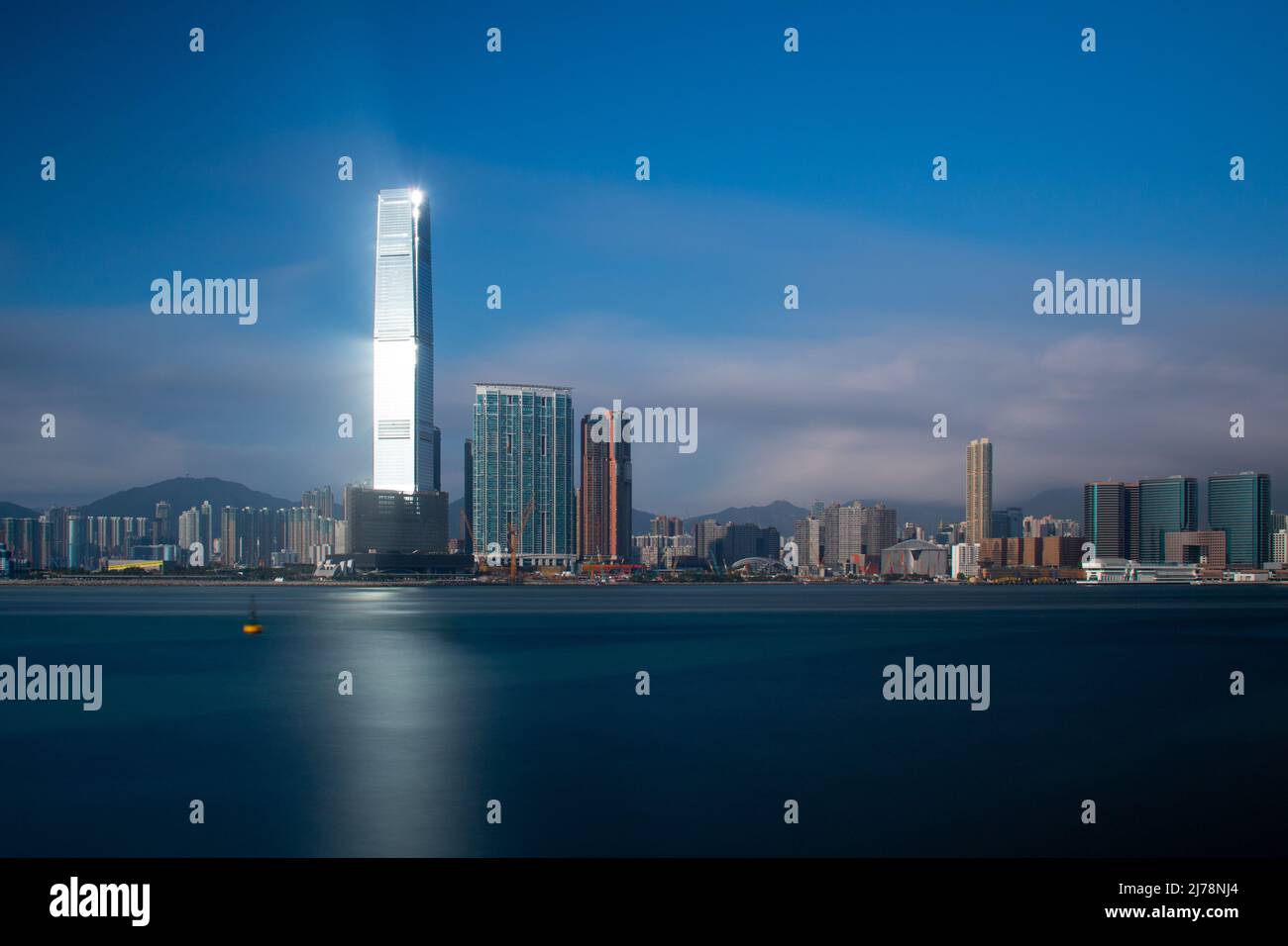Le soleil se reflète sur un gratte-ciel de Kowloon, Hong Kong jetant la lumière sur la mer bleue. Une longue exposition donne une mer douce comme de la soie. Banque D'Images