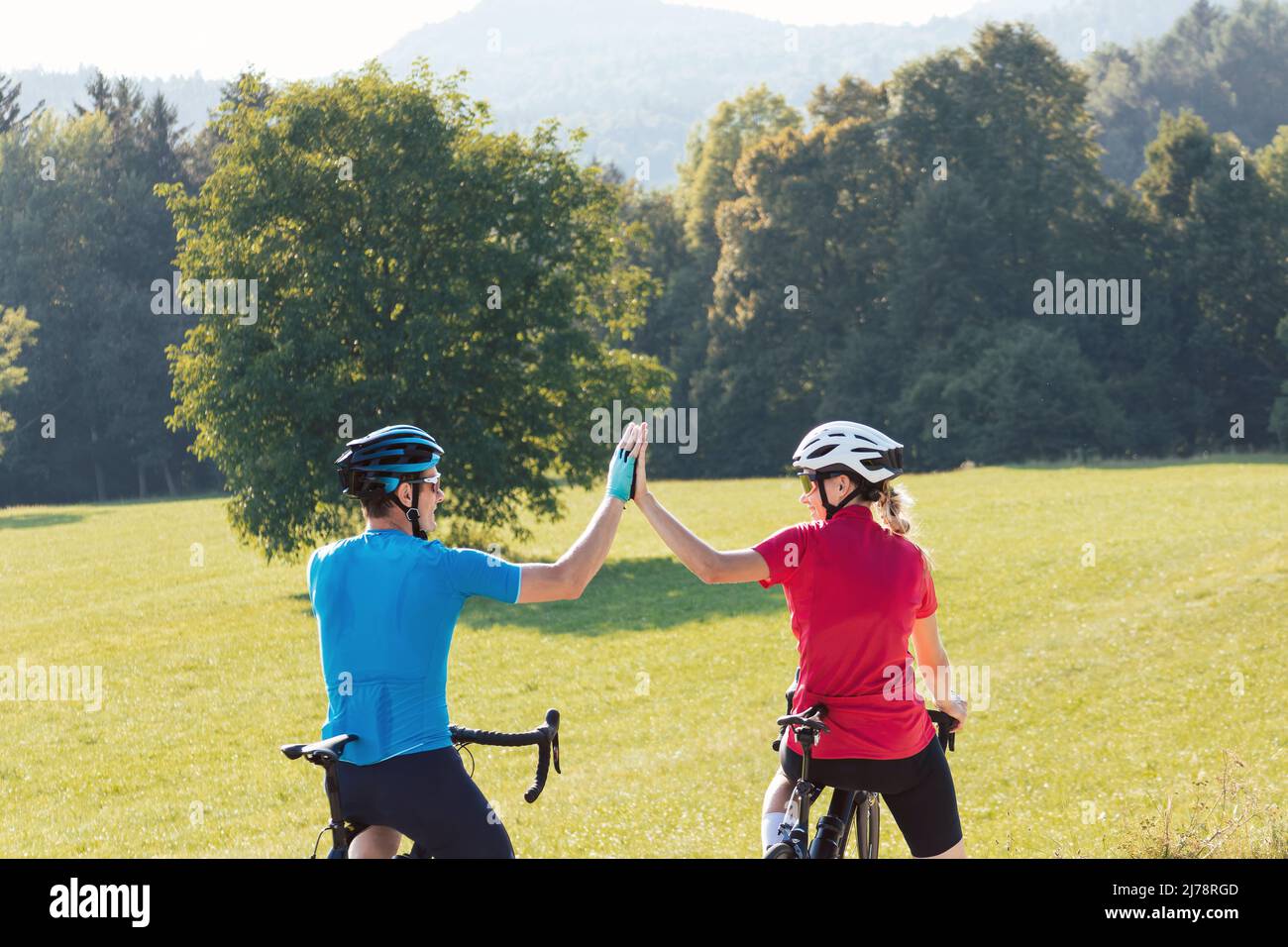 Femme et homme sur des cycles de course sur route prenant une pause après un entraînement réussi et regardant le coucher de soleil sur les montagnes donnant élevé cinq Banque D'Images