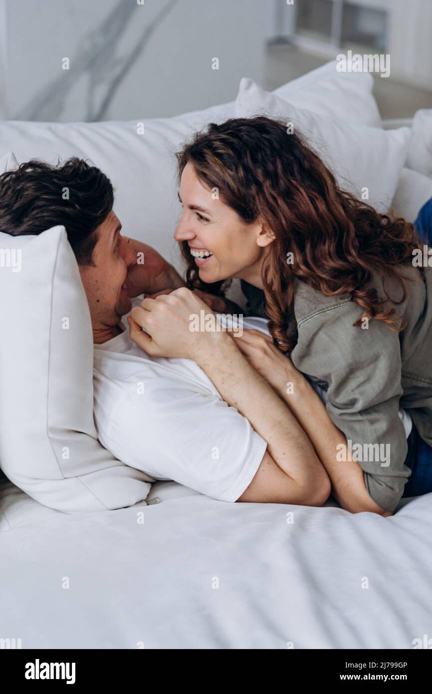 Les jeunes mariés aux cheveux foncés ont des chatouilles amusantes et embrasser allongé sur le canapé et s'embrasser doucement avec amour dans le salon de très gros plan Banque D'Images