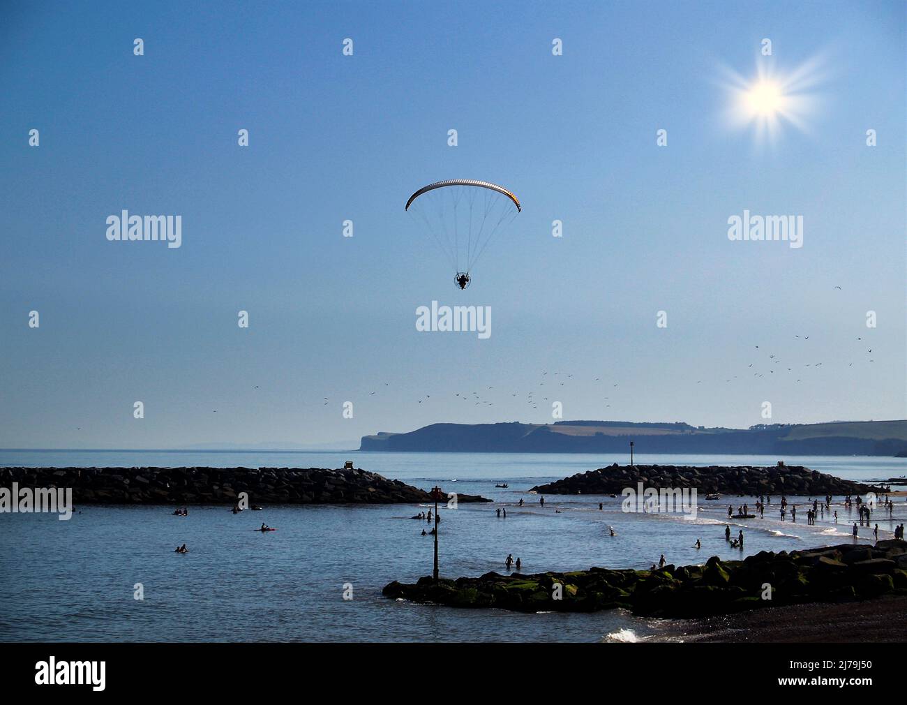 Un parapente motorisé au-dessus des rochers de Chit près de Jacobs Ladder Beach Sidmouth, East Devon pris dans le soleil rétro-éclairé. Les jeunes et les personnes âgées en dessous apprécient Banque D'Images