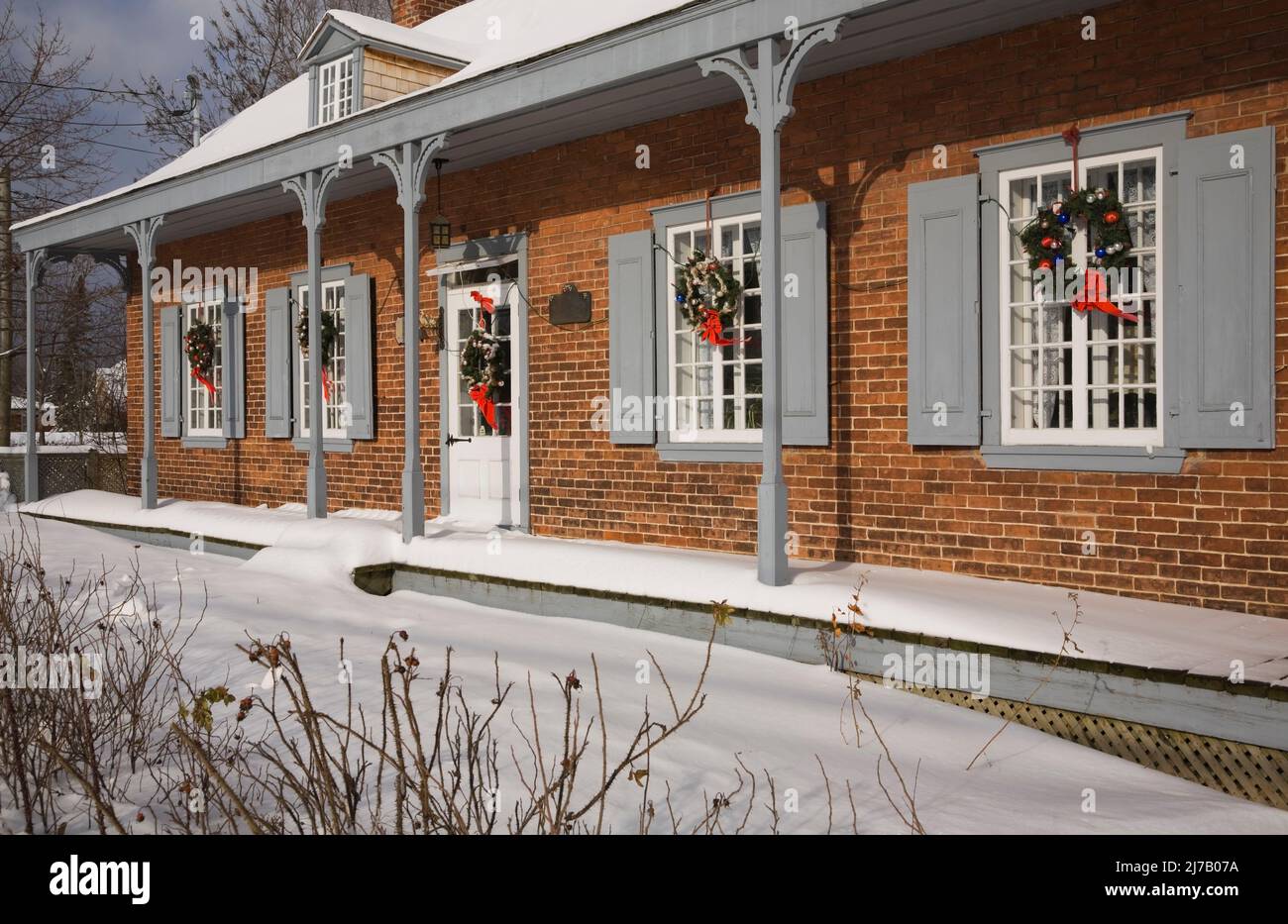 Ancienne maison en briques nuancées rouges de style Canadiana 1800s avec couronnes de Noël sur la façade en hiver. Banque D'Images