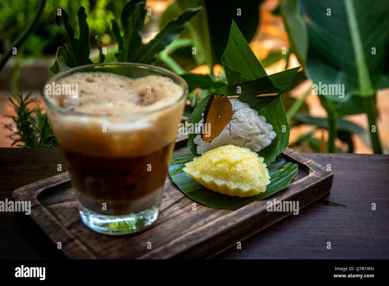 Un papillon repose à côté d'un verre de café glacé vietnamien. Banque D'Images