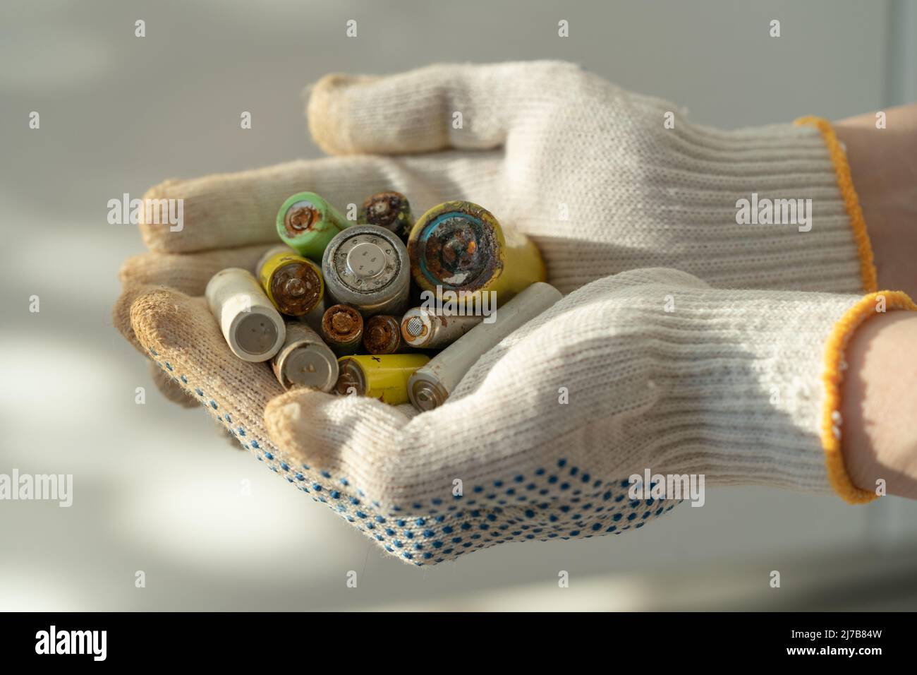 Gros plan des mains des femmes dans des gants de protection en coton tenant le tas de piles alcalines usagées Banque D'Images