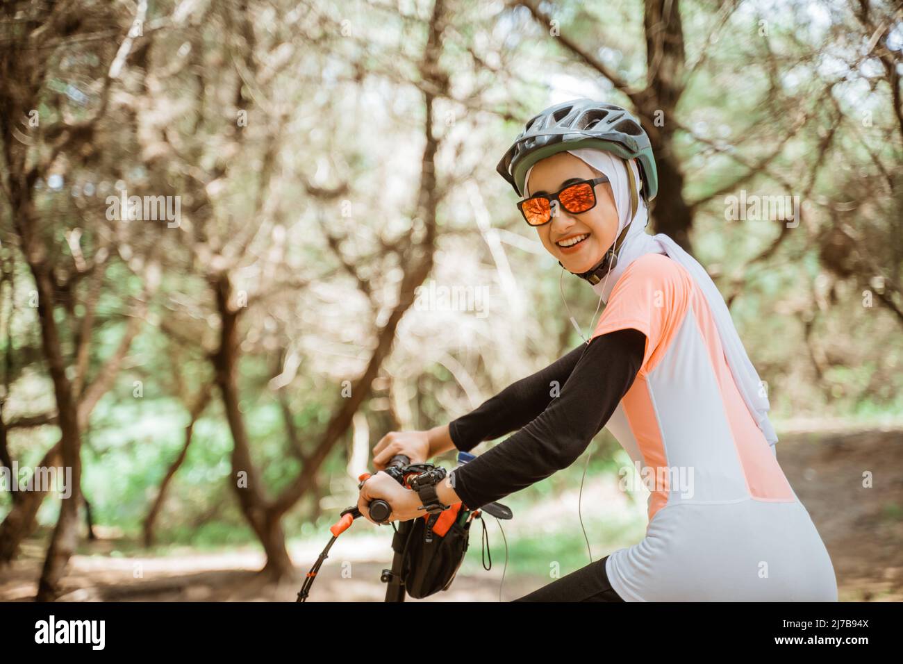 fille voilée dans des lunettes de soleil souriant portant des écouteurs à vélo dans le parc Banque D'Images