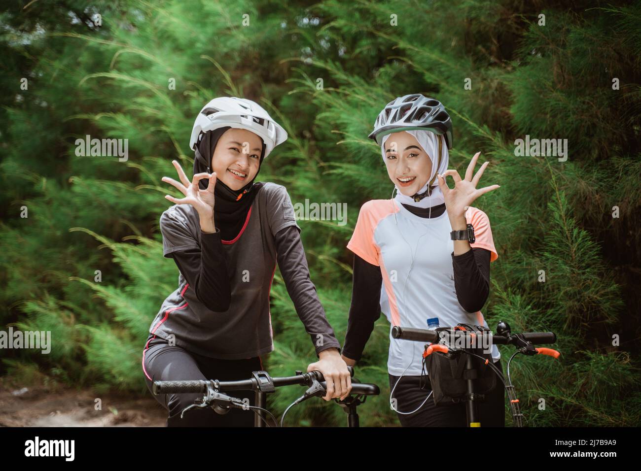 deux femmes dans le voile avec le geste de main ok tout en faisant du vélo Banque D'Images