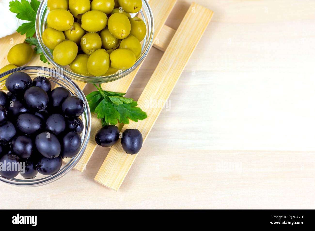 Beaucoup d'olives entières marinées dans le bol en verre avec un espace de copie sur fond de bois clair dans la vue sur le dessus de la cuisine. Banque D'Images