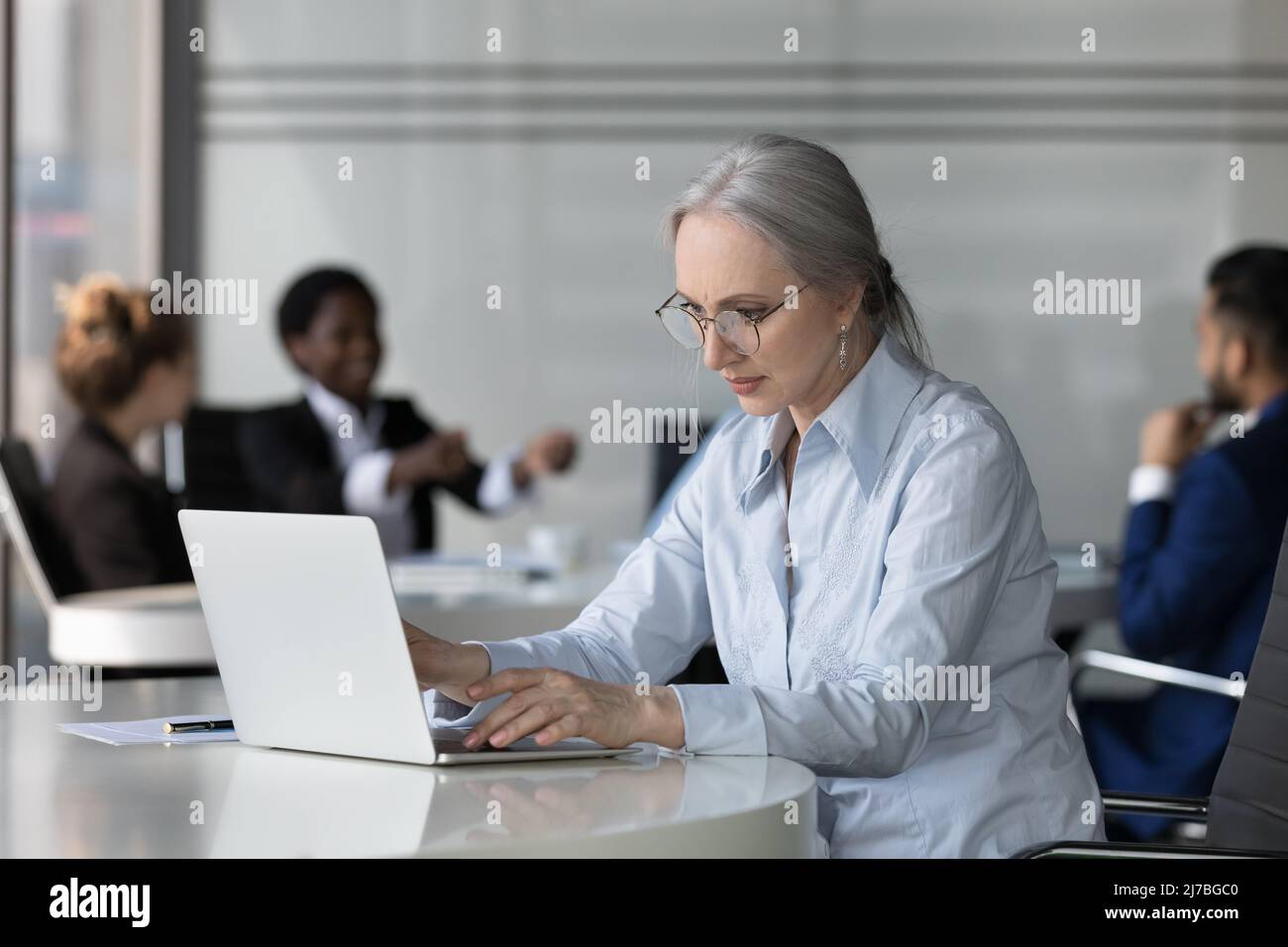 Femme professionnelle d'âge moyen concentrée dans des lunettes utilisant un ordinateur portable Banque D'Images