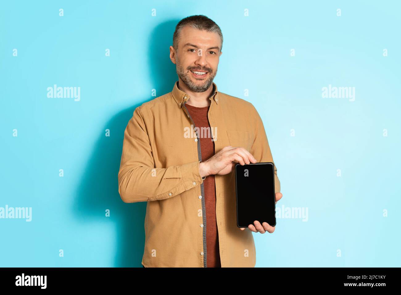Un freelancer masculin montre une tablette avec écran vide sur fond bleu Banque D'Images