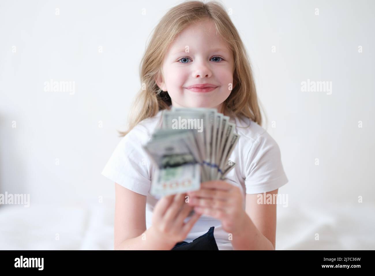Souriant belle petite fille tient le ventilateur de dollars. Banque D'Images