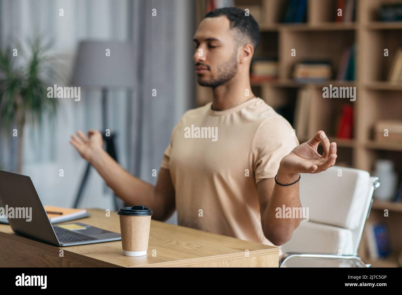 Concept de soulagement du stress au travail. Homme arabe calme méditant devant un ordinateur portable à la maison, assis sur le lieu de travail Banque D'Images