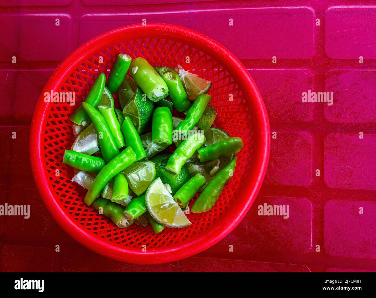 Poivrons verts coupés en tranches dans un bol rouge à côté des limes coupées. Banque D'Images