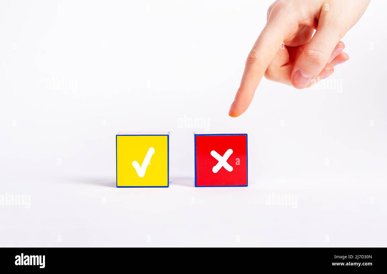 Choix entre décisions positives et négatives, concept de vote. Index pointant vers un cube rouge avec une croix au lieu d'un cube jaune avec une marque de graduation. Rejet, désapprobation. Photo de haute qualité Banque D'Images