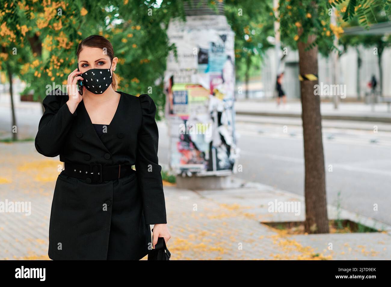 Femme de direction portant un masque de visage tout en parlant au téléphone à l'extérieur dans la rue. Banque D'Images