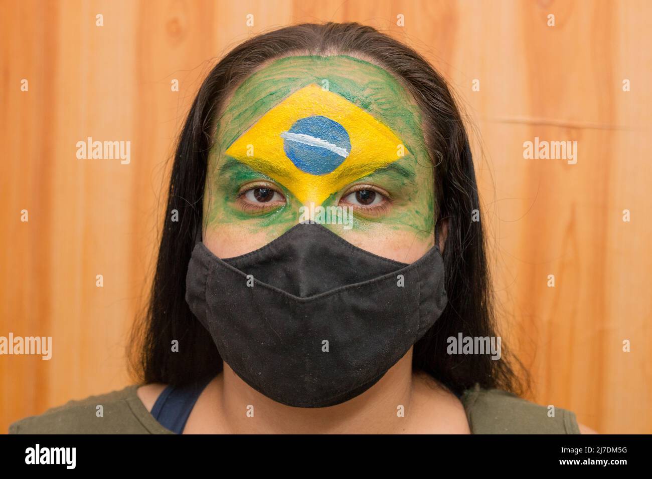 Femme avec le drapeau du Brésil peint sur son visage avec un masque noir à Rio de Janeiro. Banque D'Images