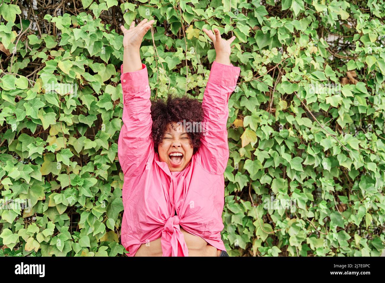 bonne jeune femme aux bras étirés. femme aux cheveux bouclés célébrant et souriant. Banque D'Images
