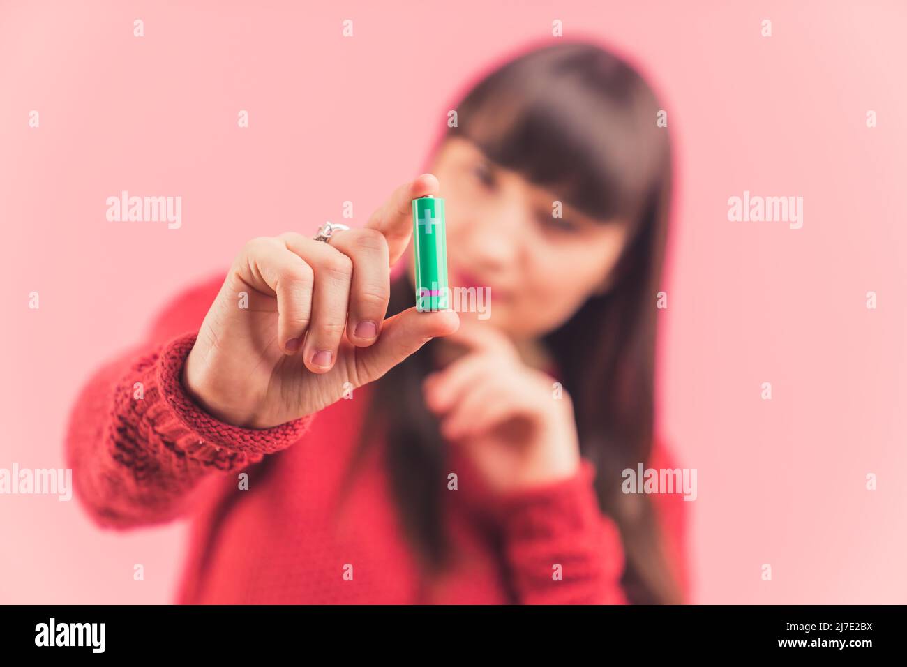 La femme caucasienne à cheveux foncés montre la batterie à la caméra arrière-plan rose copie espace studio tourné de gros plan moyen. Photo de haute qualité Banque D'Images