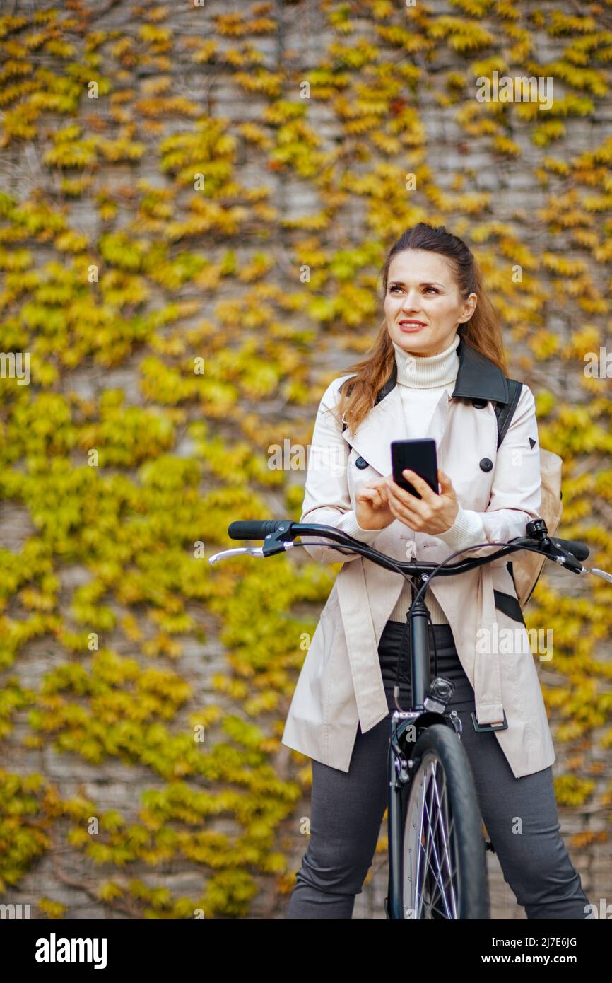 femme moderne pensive en trench-coat beige avec vélo utilisant des  applications de smartphone contre le mur vert à l'extérieur de la ville  Photo Stock - Alamy
