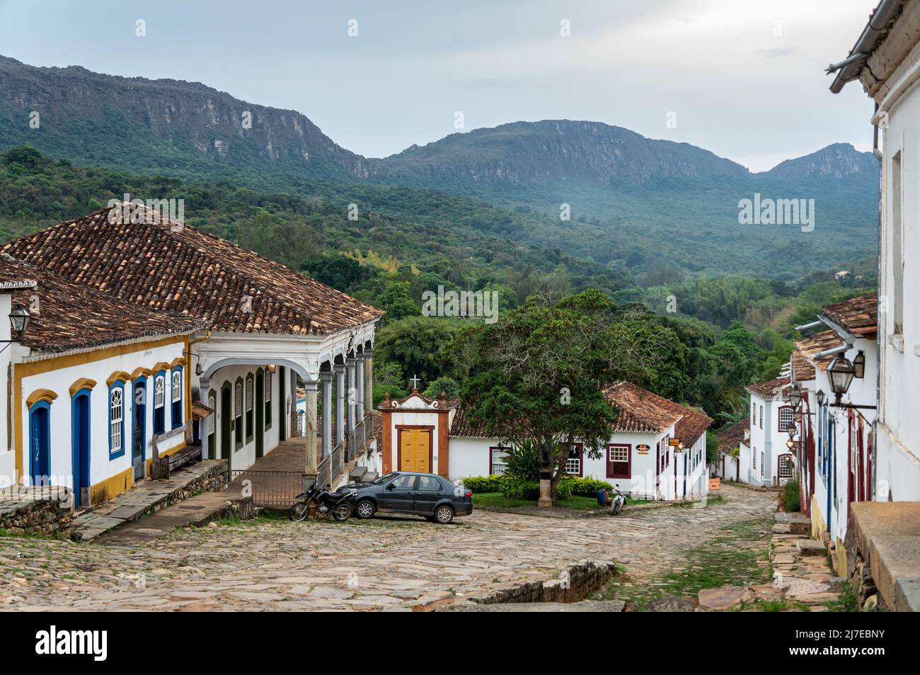 Vue panoramique sur la descente Rua da Camara rue pavée et ses maisons coloniales dans le centre historique de Tiradentes sous ciel nuageux. Banque D'Images