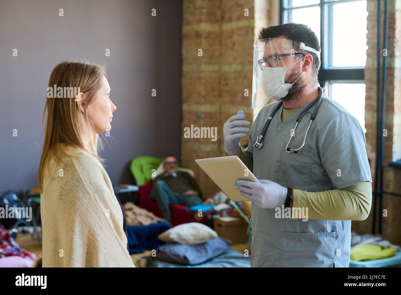 Médecin avec un comprimé donnant des conseils médicaux à une jeune réfugiée malade dans un camp et expliquant comment traiter sa maladie Banque D'Images