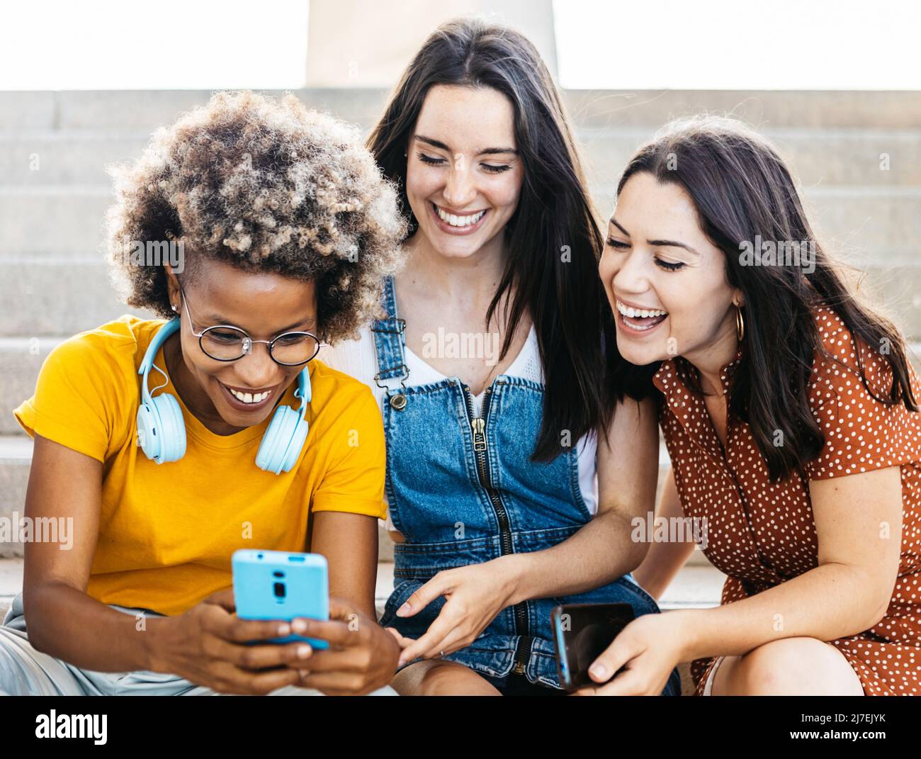 Trois amies multiraciales rient ensemble en utilisant un téléphone portable Banque D'Images