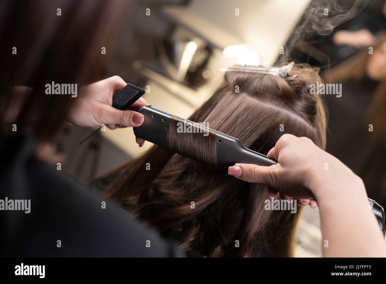 gros plan des mains du maître dans le salon de spa lissez les cheveux avec un fer à repasser dans le salon de spa. Banque D'Images