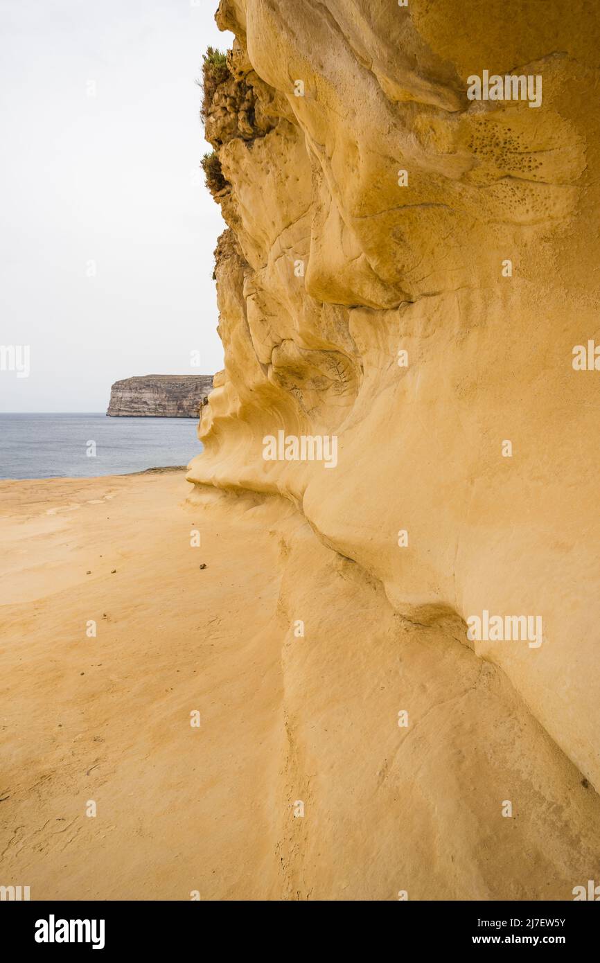 Roche jaune courbée autour de la baie de Xlendi sculptée par des années de vagues écrasées sur l'île de Gozo à Malte. Banque D'Images