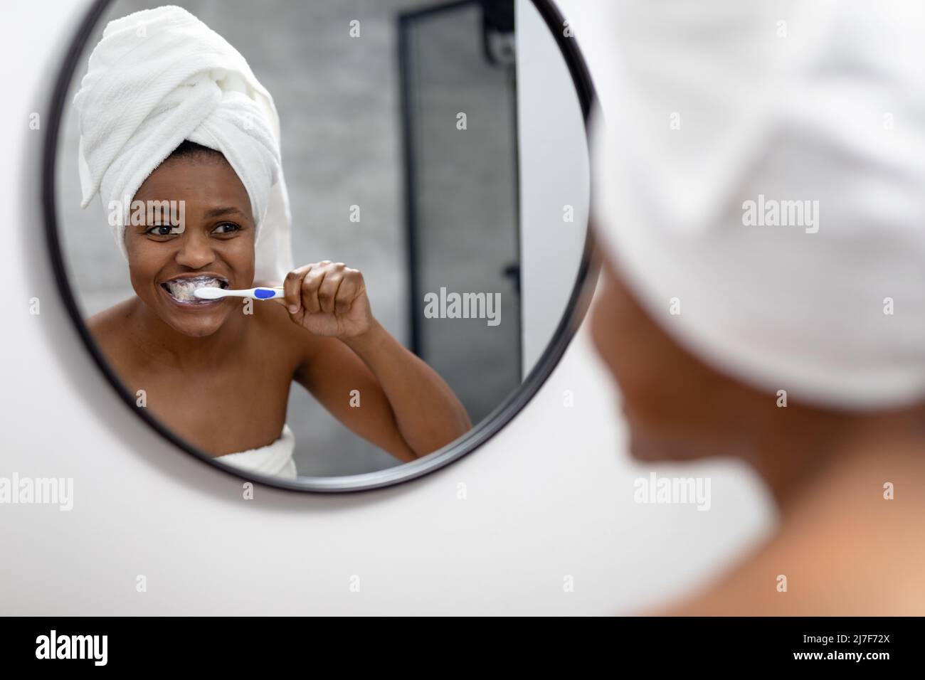 Afro-américaine femme adulte de taille moyenne regardant le miroir et se brossant les dents dans la salle de bains Banque D'Images