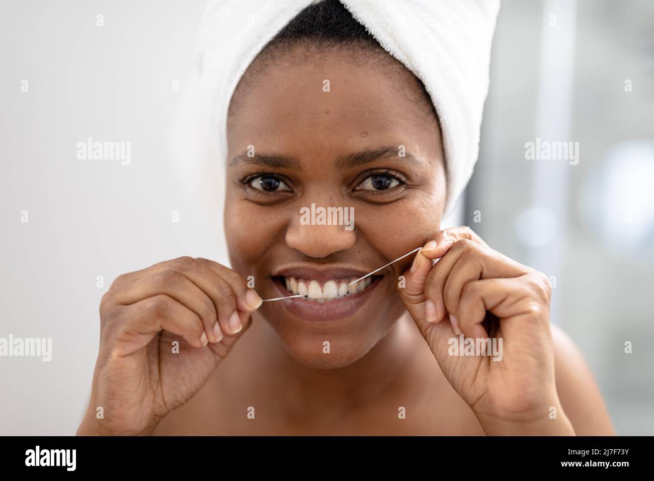 Portrait d'une femme afro-américaine de taille moyenne utilisant de la soie dentaire dans la salle de bains Banque D'Images